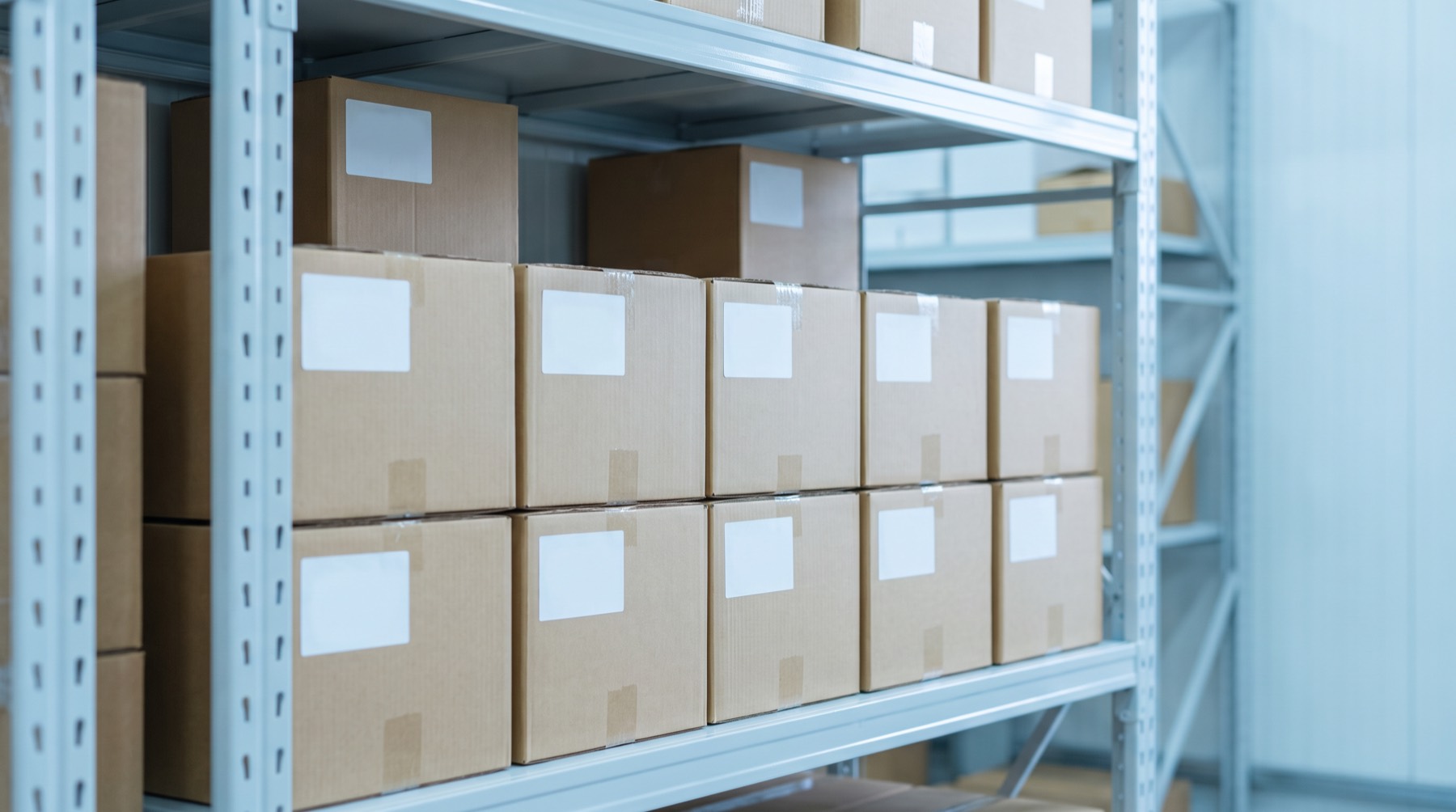 Plain cardboard boxes with blank labels stacked neatly on a warehouse shelf